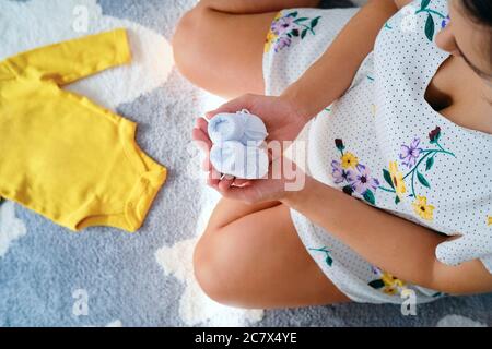 Jeune femme enceinte assise sur le sol tenant les chaussons de bébé Banque D'Images