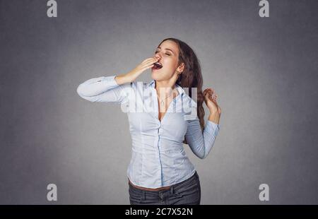 Debout belle femme bâchant et s'étirant isolé sur fond gris studio. Mannequin fille avec de longs cheveux ondulés bouclés en chemise bleue formelle. Gros plan Banque D'Images