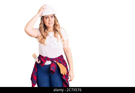 Jeune femme caucasienne portant un casque de sécurité, embrouillent et se demandent des questions. Incertain avec doute, pensant à la main sur la tête. Concept pensif. Banque D'Images