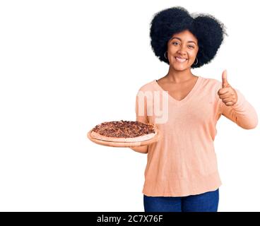 Jeune fille afro-américaine tenant une pizza italienne souriante et positive, pouce vers le haut faisant excellent et signe d'approbation Banque D'Images