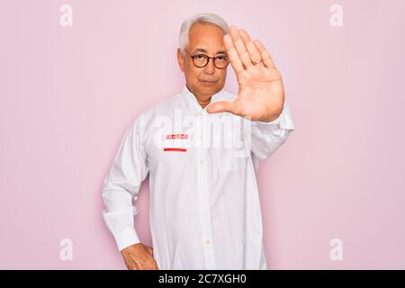 Homme âgé de milieu de vie à cheveux gris portant bonjour mon nom est l'introduction autocollant avec main ouverte faire signe stop avec une expression sérieuse et confiante, Banque D'Images