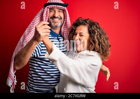 Un beau couple d'âge moyen porte un foulard arabe et un sweat-shirt souriant heureux et confiant. Se tenant avec le sourire sur le visage embrassant sur isolé rouge b Banque D'Images