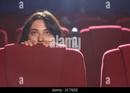 Portrait d'une jeune femme effrayée se cachant derrière le siège tout en regardant un film d'horreur dans un cinéma vide, espace de copie Banque D'Images