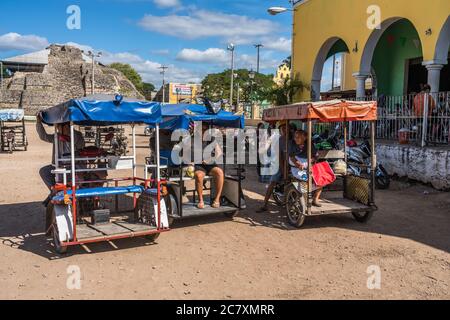 Pssengers en moto-taxis devant le marché à Acanceh, Yucatan, Mexique. Derrière se trouvent les ruines d'une pyramide maya Banque D'Images