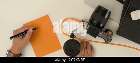 Photo en tête d'un photographe masculin prenant note sur le bloc-notes et tenant une tasse de café sur un bureau blanc Banque D'Images