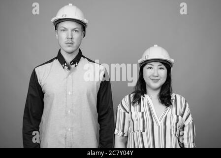 Jeune homme d'affaires élégant et femme d'affaires asiatique mature portant un casque sur fond gris Banque D'Images