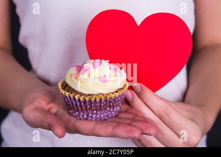 concept de la saint-valentin : gâteau au beurre doux et coloré et cœur rouge entre les mains des femmes Banque D'Images