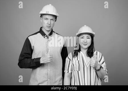 Jeune homme d'affaires élégant et femme d'affaires asiatique mature portant un casque sur fond gris Banque D'Images