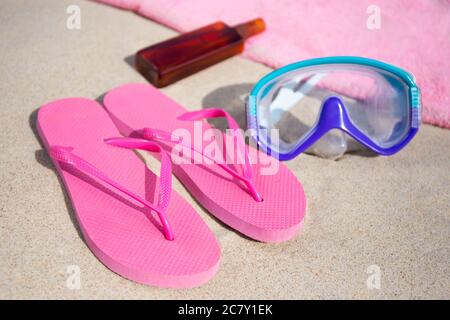 concept été - tongs roses, serviette, masque de plongée et bouteille de lotion de bronzage sur la plage de sable Banque D'Images