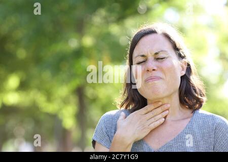Femme d'âge moyen en douleur souffrant d'un mal de gorge dans le parc en été Banque D'Images