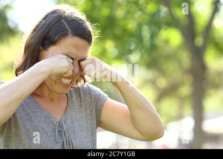 Femme d'âge moyen se grattant les yeux qui s'démangent debout dans un parc en été Banque D'Images