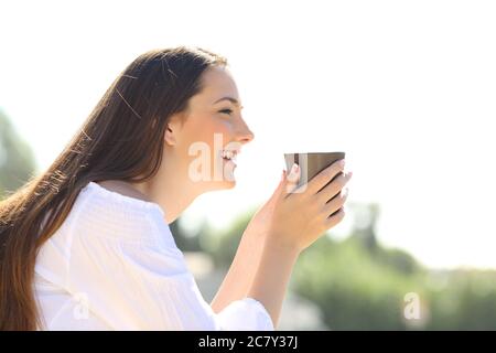 Vue latérale d'une femme heureuse tenant une tasse de café, vue à l'extérieur contemplant des vues Banque D'Images