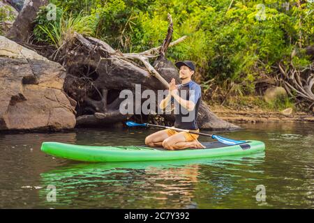 Homme pratiquant le yoga sur un panneau SUP au lever du soleil sur une grande rivière. Stand up paddle board - des loisirs dynamiques dans la nature Banque D'Images