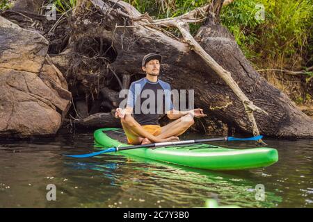 Homme pratiquant le yoga sur un panneau SUP au lever du soleil sur une grande rivière. Stand up paddle board - des loisirs dynamiques dans la nature Banque D'Images