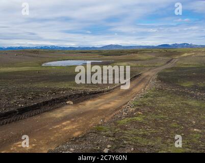 Route de montagne de terre dans le paysage vert abandonné à la réserve naturelle de Fjallabak en Islande avec la chaîne de montagne couverte de neige rhyolit, ciel bleu nuages blancs Banque D'Images