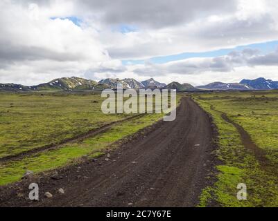 Vue sur la route de montagne de terre F210 dans le paysage vert abandonné à la réserve naturelle Fjallabak en Islande avec la neige colorée couverte de montagnes rhyolit, bleu Banque D'Images