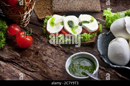 assemblage du sandwich avec mozzarella, tomates fraîches, sauce pesto et salade de laitue verte, sur table rustique en bois, personne Banque D'Images