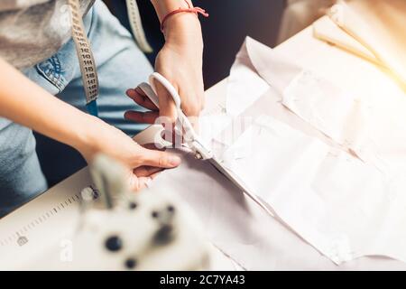 motif, ciseaux, mètre à ruban et machine à coudre. Lieu de travail de couturière. La couturière coupe le détail de la robe sur les lignes d'esquisse. Banque D'Images