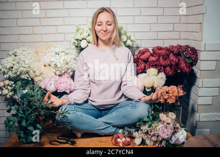 Belle fille en robe rose tendre avec bouquet de fleurs pivoines dans les mains assis sur la table contre fond floral dans la boutique de fleurs. Banque D'Images