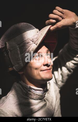 Homme portant un costume d'escrime pratiquant avec une épée contre une vignette grise Banque D'Images