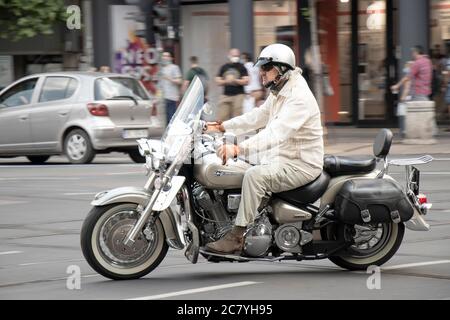 Belgrade, Serbie - 16 juillet 2020 : homme mature en costume beige clair, à cheval sur une moto à double siège avec sacs à selle latéraux sur la circulation urbaine, côté v Banque D'Images
