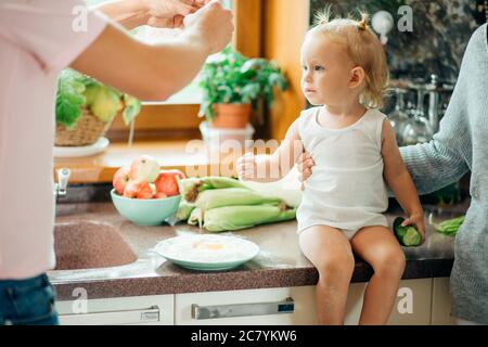 Jeune couple avec enfant s'amuser dans la cuisine tout en préparant la salade de légumes Banque D'Images