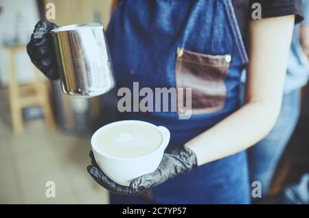 La femme tient un pot à lait et une tasse de café, prépare un cappuccino, verse du lait fouetté dans un espresso.image floue, mise au point sélective Banque D'Images