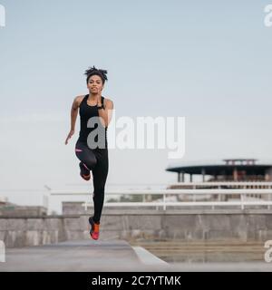 Courir avec des sauts en entraînement. Fille afro-américaine en uniforme de sport à sauter, au stade Banque D'Images