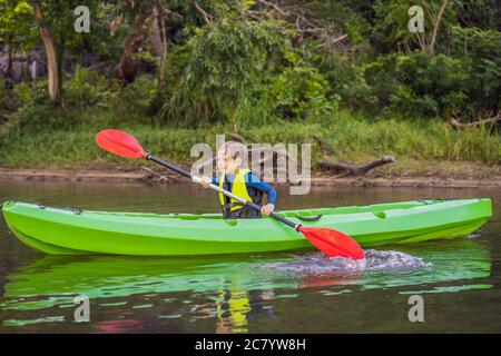 Joyeux jeune garçon tenant la pagaie dans un kayak sur la rivière, profitant d'une belle journée d'été Banque D'Images