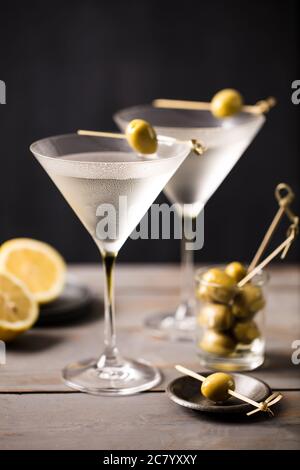 Cocktails martini frais servis avec un décor olive sur un bar en bois gris à fond sombre Banque D'Images