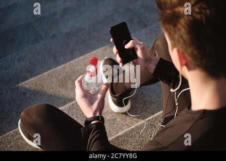 Gros plan d'un jeune sportif avec une bouteille d'eau à l'aide d'un téléphone portable extérieur Banque D'Images