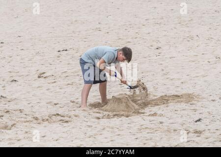 Un jeune vacanciers utilisant une bêche pour construire un château de sable sur la plage de Fistral à Newquay, en Cornouailles. Banque D'Images