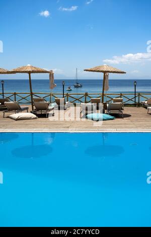 Chaises longues avec parasol près d'une piscine bleu clair à côté de la plage à Skopelos avec une atmosphère de vacances ensoleillée. Banque D'Images