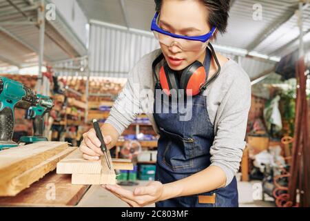 Menuisier professionnel féminin en lunettes de protection, dessin de marques sur panneau de bois avant de le couper Banque D'Images