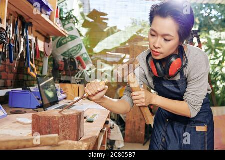 Charpentier vietnamien concentré utilisant le burin et le marteau pour sculpter le bois Banque D'Images