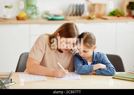 Portrait ton chaud de mère attentionnée aidant la fille à faire ses devoirs et à étudier à la maison dans un intérieur confortable, espace de copie Banque D'Images