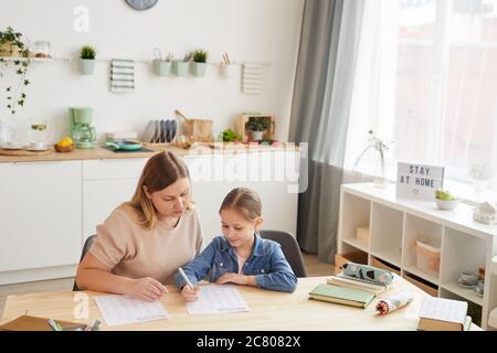 Vue en grand angle sur la mère bienveillante aidant une jolie fille à faire ses devoirs et à étudier à la maison dans un intérieur confortable, espace de copie Banque D'Images