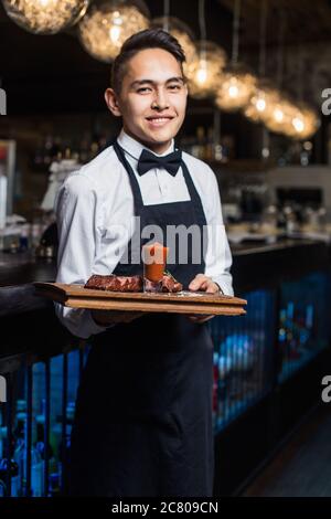 Gros plan de la main du serveur en notant le menu sur la tablette. Jeune femme commandant de la nourriture à un serveur au restaurant. Jeune belle femme pensant à la nourriture à Banque D'Images