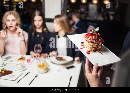 Gros plan de la tranche de gâteau au chocolat sur une assiette blanche tenue par une femme plus âgée en haut bleu et en foulard (mise au point sélective) Banque D'Images