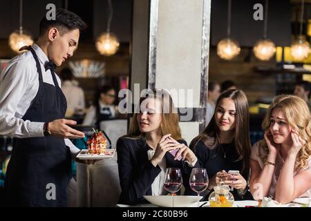 Gros plan de la main du serveur en notant le menu sur la tablette. Jeune femme commandant de la nourriture à un serveur au restaurant. Jeune belle femme pensant à la nourriture à Banque D'Images