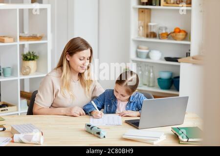 Portrait d'une femme adulte souriante aidant une fille à faire ses devoirs ou à étudier à la maison dans un intérieur confortable, espace de copie Banque D'Images