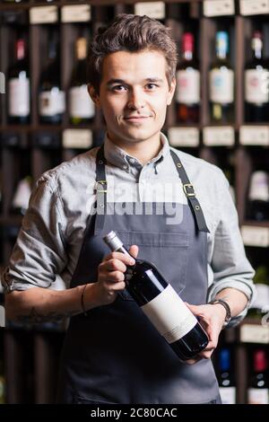 Portrait d'un sommelier debout dans une cave à vin tenant un verre de vin et montrant le pouce vers le haut, pendant une dégustation Banque D'Images