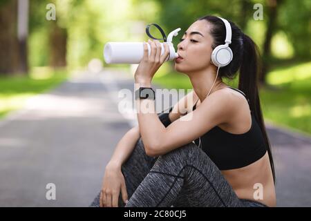 Soif après l'entraînement. Jeune fille asiatique buvant de l'eau, se reposant après des hors-soors de jogging Banque D'Images