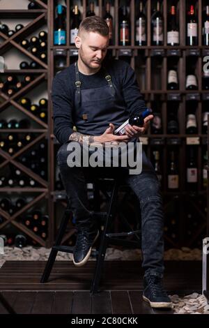 Portrait d'un sommelier debout dans une cave à vin tenant un verre de vin et montrant le pouce vers le haut, pendant une dégustation Banque D'Images