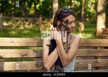 Une fille avec son chien est assise sur un banc de parc. Petit chien du Yorkshire Terrier dans les bras de son propriétaire. Banque D'Images