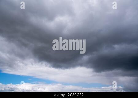 Nuages sombres avec pluie accrochée sur un ciel bleu vif lors d'une journée avec le temps changeant Banque D'Images