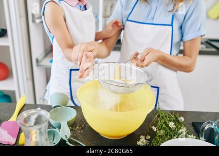 Mère enseignant à la fille comment tamiser la farine dans un bol en utilisant un tamis pour faire de la pâte pour la pâtisserie ou la pizza Banque D'Images