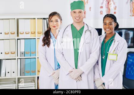 Portrait de jeunes médecins heureux debout dans le bureau médical et souriant à la caméra Banque D'Images