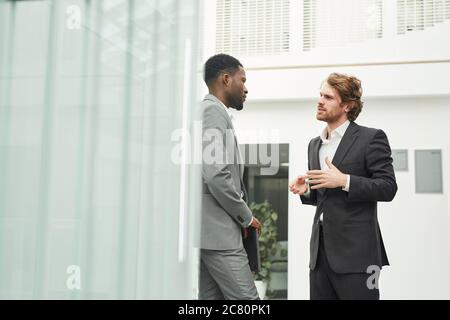 Portrait de deux hommes d'affaires prospères portant des costumes discutant à l'extérieur près d'un immeuble de bureaux, espace de copie Banque D'Images