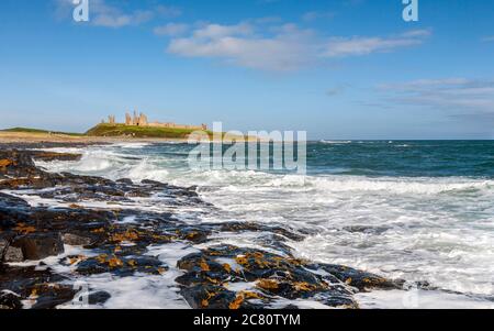 Vagues se brisant sur les rochers ignés noirs du château de Dunstanburgh, Northumberland, Angleterre Banque D'Images